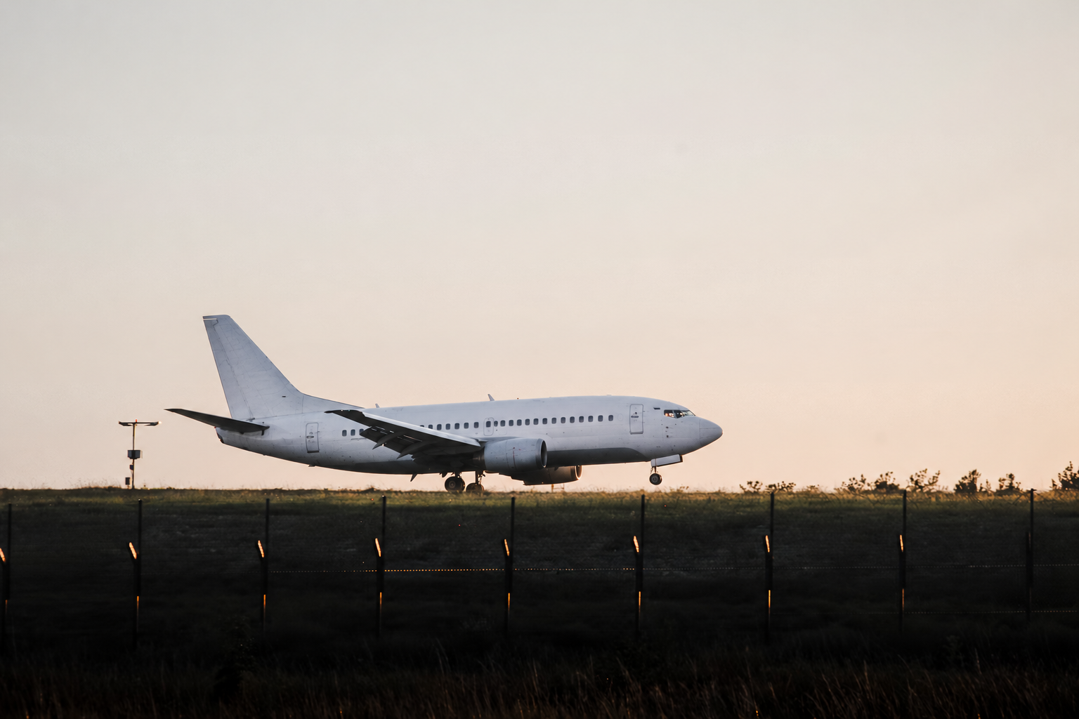 An unbranded passenger aircraft moving across a runway at sunset
